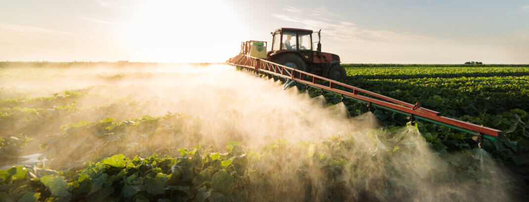 Ein Landwirt benutzt auf einem Traktor ein Zerstäubungssystem zum Besprühen von Nutzpflanzen.