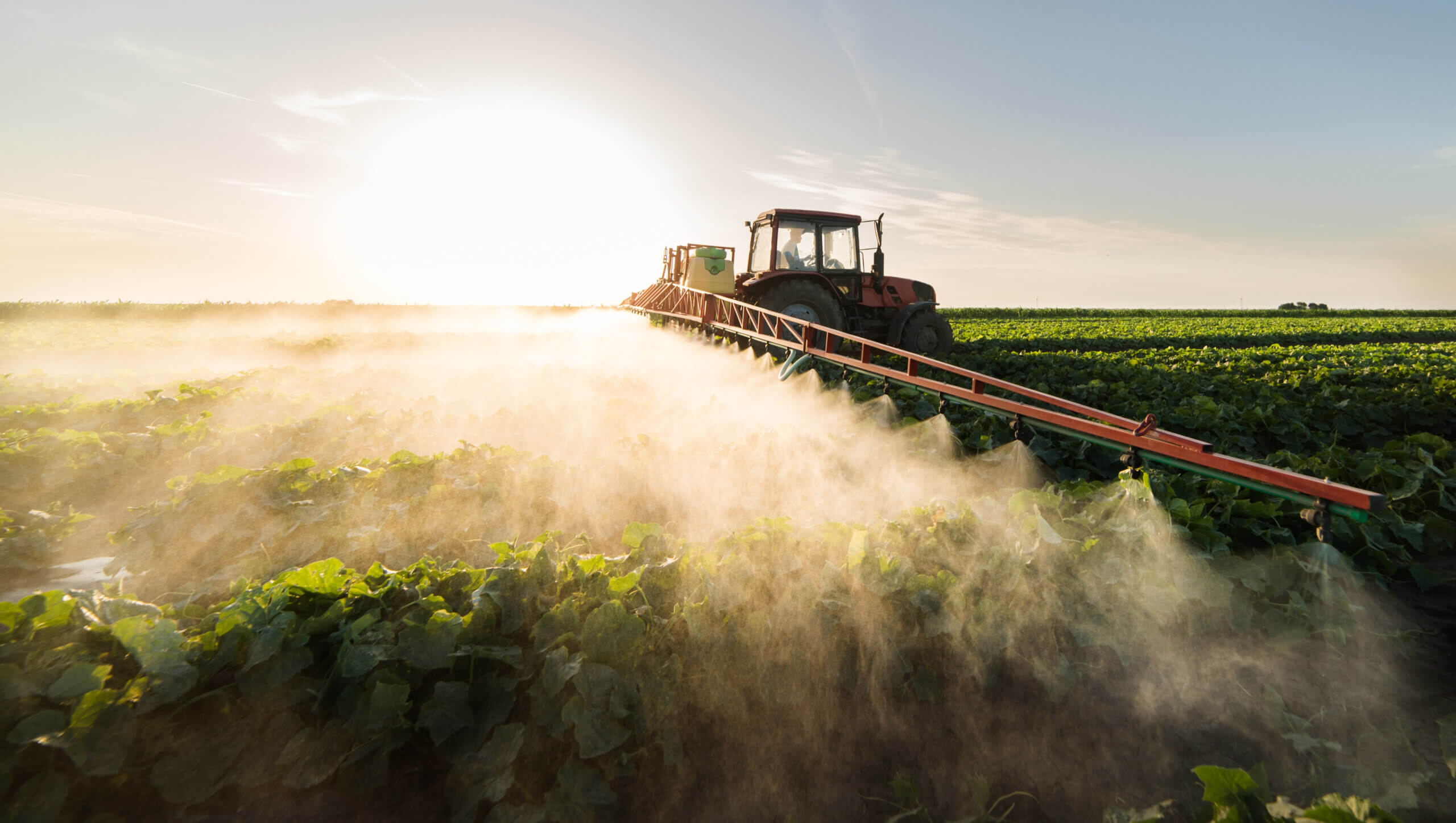 Ein Landwirt benutzt auf einem Traktor ein Zerstäubungssystem zum Besprühen von Nutzpflanzen.